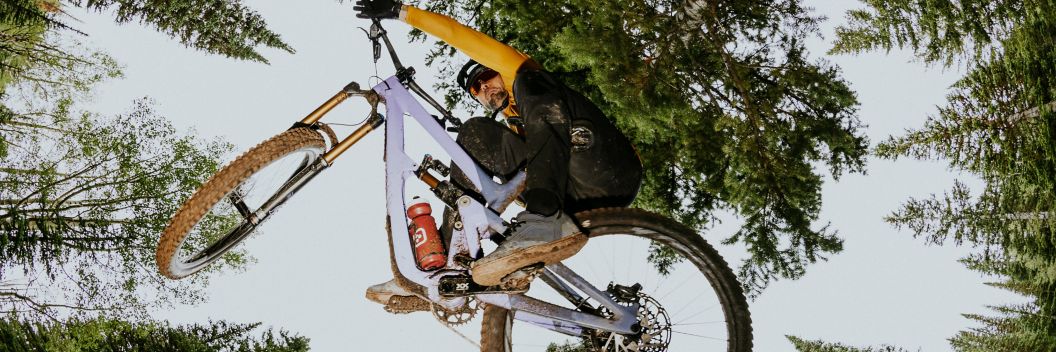 2023 Mountain Bike Guide text on an image looking up at an MTB rider in fall apparel table-topping in an alpine tree forest.